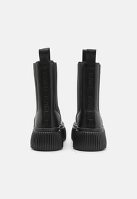 Bottines noires en cuir lisse, avec une semelle striée et des panneaux élastiques sur les côtés, dotées d'onglets de tirage avec logo à l'arrière.