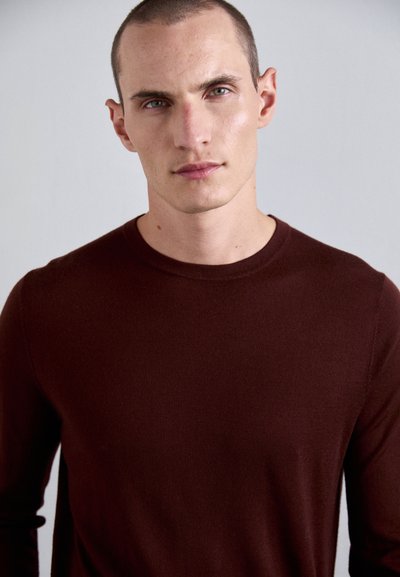 Pulover lung cu maneci burgundy, realizat dintr-un material moale, cu guler rotund și design ajustat, având o textură netedă și cusături minime.