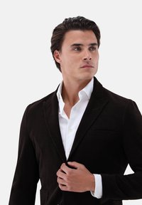 Braune Cordcordjacke mit strukturiertem Design, ausgestattet mit einem Reverskragen und einer Brusttasche, kombiniert mit einem weißen Hemd mit Knopfleiste.