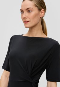 Robe noire avec un col rond, des manches courtes et un détail torsadé à la taille. Fabriquée dans un tissu lisse avec une silhouette ajustée et élégante.