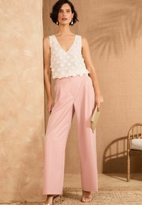 Top bianco senza maniche con accenti circolari testurizzati, abbinato a pantaloni palazzo rosa chiaro. Elegante pochette oro e tacchi nudi.