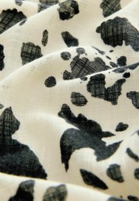 Tissu à motif noir et blanc avec une surface texturée, présentant des formes irrégulières et tachetées sur un matériau léger et transparent.