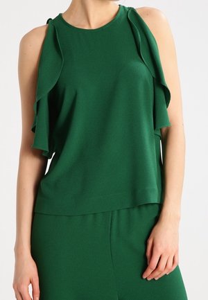 Ærmeløs mørkegrøn top med flæsepaneler på skuldrene, båret med matchende grønne bukser, vist fra nakke til hofter.