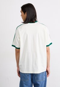 Short-sleeve white cotton t-shirt with green trim on sleeves and neck. Features a relaxed fit and raglan-style shoulder design.