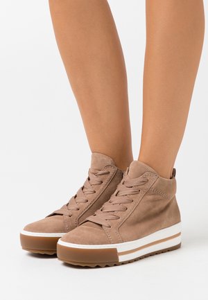 Beige mockasinliknande högklackade sneakers med rundade tår, strukturerade snören och en vit mellansula med en brun rand. Gummisula ger bra grepp.