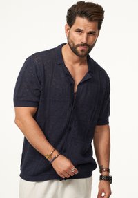 Navy gestricktes Kurzarmhemd mit offenen Mustern, einem Kragen und vorderen Knöpfen. Strukturiertes Gewebe mit lockerer Passform.