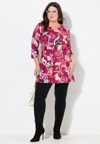 Tunika floreale con maniche a tre quarti nelle tonalità di fucsia e rosa, abbinata a leggings neri e stivaletti. Accessorio borsa bianca.