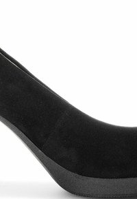 Escarpin en daim noir à talon haut avec un bout rond et un talon compensé épais. Texture lisse avec des coutures minimales, comportant un design supérieur sans couture.