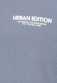 Graues Baumwoll-T-Shirt mit weißem Text: "URBAN EDITION THE SUBLEVEL CLOTHING BRAND ONLY THE REAL ONES" in einer kräftigen, modernen Schriftart.