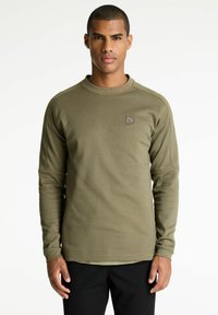 Camisa de manga larga verde oliva hecha de tejido texturizado, con cuello redondo y un pequeño parche con logo en el lado izquierdo del pecho.