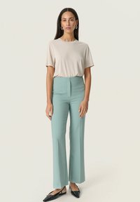 Lys beige kortærmet T-shirt parret med højtaljede, brede mintgrønne bukser og sorte spidse flade sko.