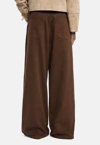 Szerokie brązowe spodnie wykonane z denimu, charakteryzujące się gładką teksturą, dwoma tylnymi kieszeniami z widocznym przeszyciem oraz luźnym krojem.