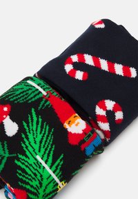 Pestré ponožky s černým základem a vánočními motivy jako Santa Claus, houbami a cukrovinkami na tmavě modrém pozadí.