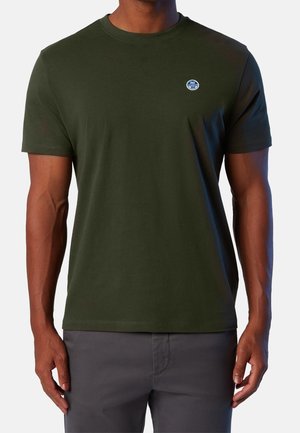 Mann trägt ein einfarbiges dunkelgrünes Kurzarm-T-Shirt mit einem kleinen runden blau-weißen Logo auf der linken Brust.