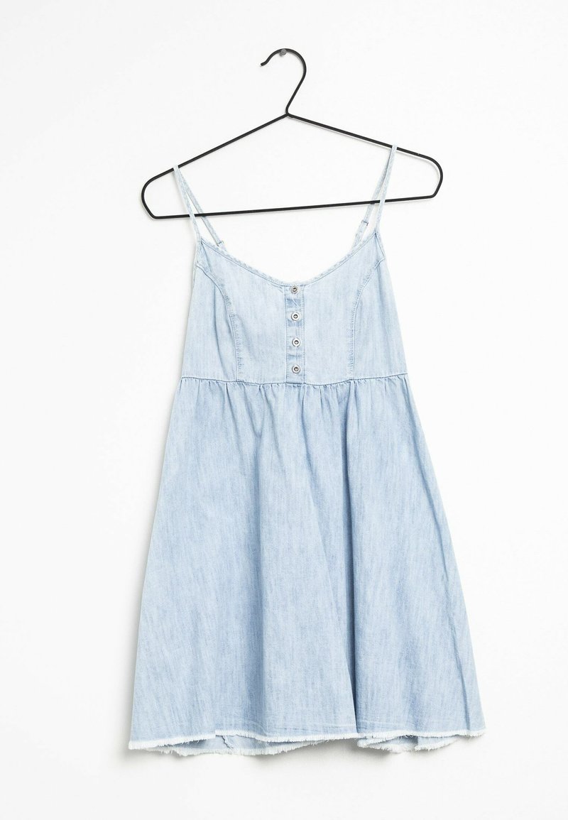 Ljust blå denimklänning med spaghettiaxlar, knappritning fram och ett lager-på-lager, flödande design; fransad fåll ger textur. Hänger på en svart krok.