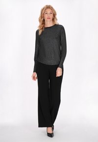 Fekete, hosszú ujjú felső fénylő textúrával, széles szárú fekete nadrággal és fekete cipővel párosítva. Az öltözék kerek nyakkivágással rendelkezik.