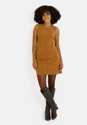 Vestido de pana marrón con forma ajustada y escote redondeado, combinado con botas altas marrones hasta la rodilla. Textura suave en toda la prenda.