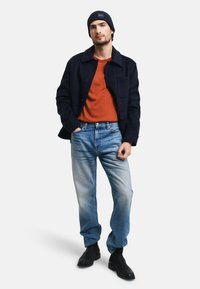 Granatowa wełniana kurtka w połączeniu z pomarańczowym t-shirtem, jasnoniebieskimi dżinsami i czarnymi botkami za kostkę. Stylizację uzupełnia żeberkowa granatowa czapka.