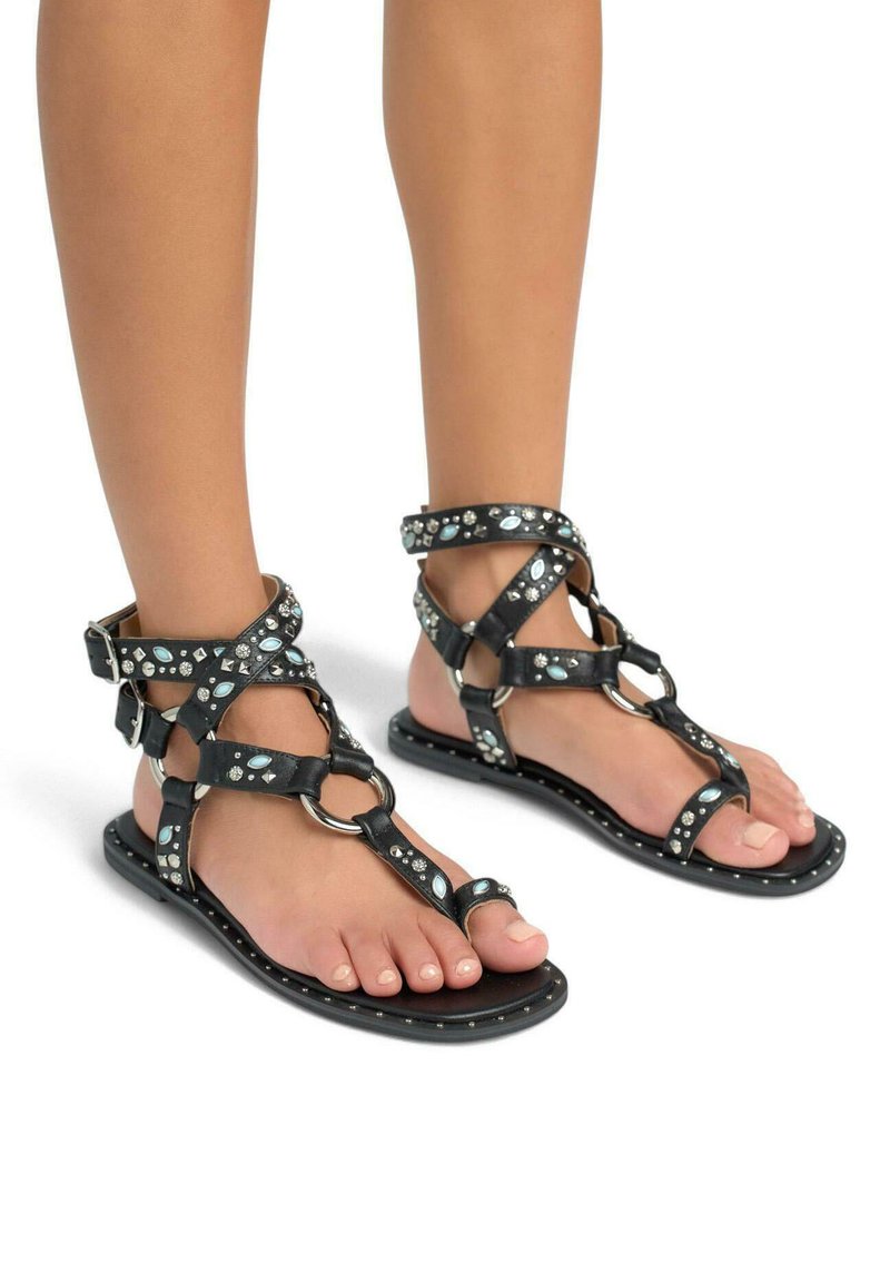 Czarne skórzane sandały z krzyżującymi się paskami, ozdobami w kolorze srebrnym i turkusowym, zapięciami na kostkę oraz płaską podeszwą. Otwarta konstrukcja palców.