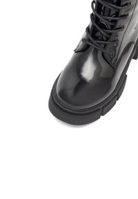 Mustad musta lakitud nahast pahkluu saapad ümmarguse varbaga, paksu kummitald ja mustad paelad, millel on sile, läikiv pind ja vastupidav disain.