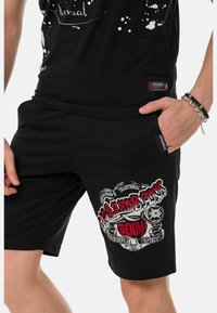 Schwarze Shorts mit einem auffälligen Grafikdruck in Weiß und Rot, aus strukturiertem Stoff und mit seitlichen Taschen für Funktionalität.