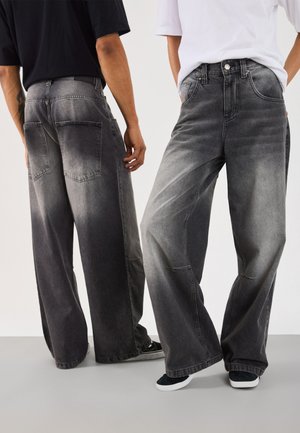 Wide-leg, dark gray denim jeans with faded accents, featuring back pockets and contrasting stitching details, worn with casual shoes.