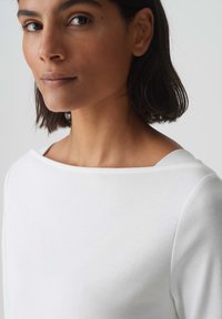 Witte lange mouwen top met een brede, boot halslijn. Soepele katoenen textuur met schone stiksels en een losse pasvorm, die een minimalistisch ontwerp laat zien.