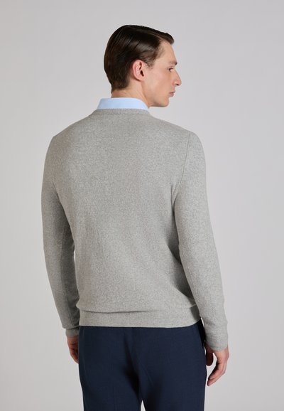 Suéter gris de punto con cuello redondo, mangas largas y puños acanalados. Llevado sobre una camisa azul clara con cuello, mostrado desde atrás.