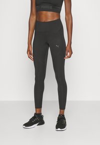 Leggings negros de cintura alta con un diseño ajustado, que presentan paneles texturizados y un pequeño logo. Llevados con zapatillas deportivas negras.