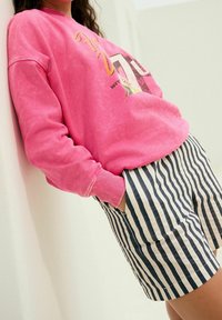 Lyserød sweatshirt med ribstrikkede manchetter og grafisk print. Kombineret med stribede marineblå og hvide shorts. Glat bomuldsstof, afslappet pasform.