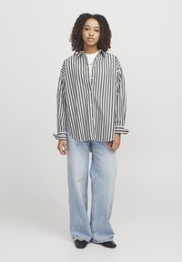 Sort og hvid stribet langærmet skjorte, oversized pasform, kombineret med lyseblå brede jeans og sorte flade sko. Enkel design, afslappet look.