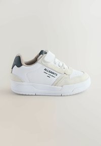 Hvid sneaker med velcrolukning, med bløde ruskindsdetaljer og en tekstureret sål. Mærkenavnet "ALLSAINTS" trykt i sort.