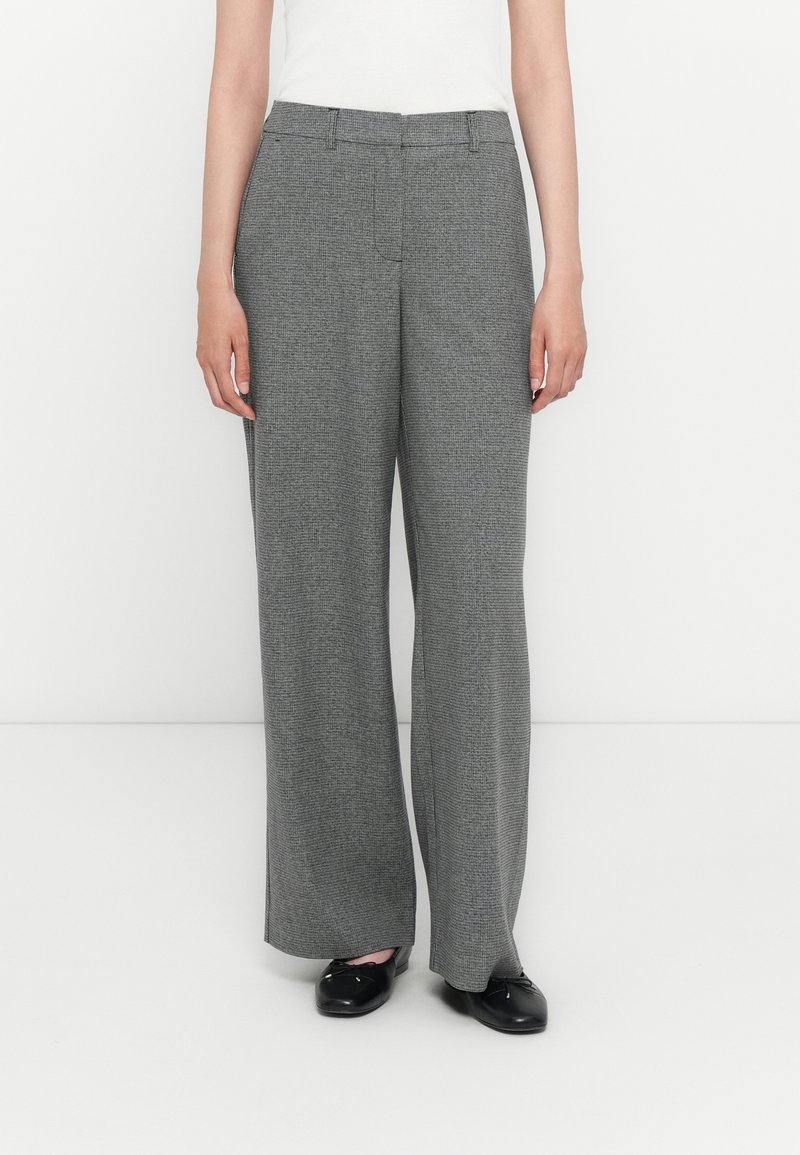 Brede broek gemaakt van een gestructureerde grijze stof, met een platte voorkant, riemlussen en een relaxte pasvorm, gestyled met zwarte schoenen.