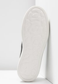 Semelle de basket noire avec un fond en caoutchouc blanc texturé, présentant un motif ondulé et la taille « 37 » embossée près du talon.