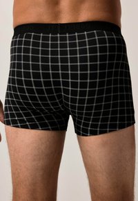 Boxer nere con un motivo a griglia di linee grigie. Presentano un elastico nero in vita con il nome del marchio, una vestibilità aderente e una texture morbida.