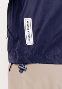 Marine vindjakke med et hvidt Armani Exchange label, elastisk snoretræk med stopper og glat, vandafvisende stof.