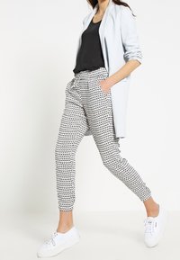 Světle modrý dlouhý blazer přes černý top, spárovaný s bílo-černými joggery s vzorem. Bílá sportovní obuv dotváří celý outfit.
