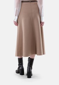 Brauner, ausgestellter Rock aus einem weichen, strukturierten Stoff. Verfügt über eine Rückennaht und wird mit kniehohen, schwarzen Stiefeln mit Absatz kombiniert.