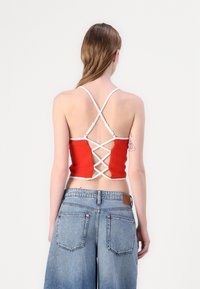 Top rouge court avec des bretelles blanches, présentant un design de dos entrecroisé. Porté avec un short en denim taille haute. Texture de tissu lisse.