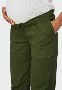 Zielone spodnie cargo z elastycznym pasem i kieszeniami. Wykonane z miękkiego materiału, z luźnym krojem, odpowiednie do noszenia w ciąży.