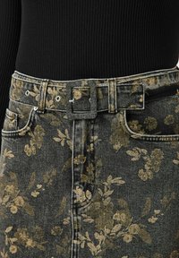 Jeans s vysokým pasem s květinovým potiskem, které mají tmavé pozadí se zlatými akcenty, stříbrnými kovovými doplňky a texturovaným páskem v pase.