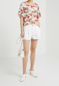 Kukkaisaiheinen lyhythihainen pusero kermanvärisenä, valkoisella pohjalla ja punaisilla kukilla. Yhdistetty valkoisiin pellavashortseihin, valkoisiin korkokenkiin ja pieneen laukkuun.