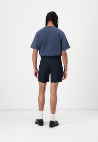 Mørkeblå shorts med en skreddersydd passform, to baklommer, kombinert med en løs, kortermet, mørk blå T-skjorte, og svarte sko med hvite sokker.