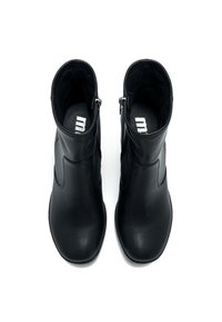 Un par de botines de cuero negro con cremalleras laterales, vistos desde arriba sobre un fondo blanco.