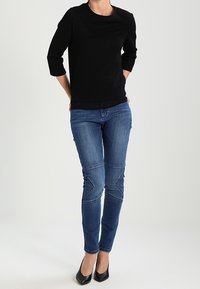 Sort tekstureret sweater med trekvartærmer, parret med blå jeans med skrå knæsyninger og sorte hæle.