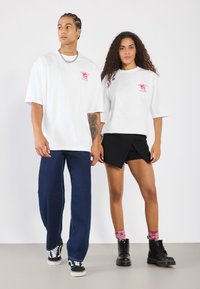 White oversized t-shirts with a pink logo, paired with blue wide-leg jeans and black shorts, complemented by black boots and patterned socks.