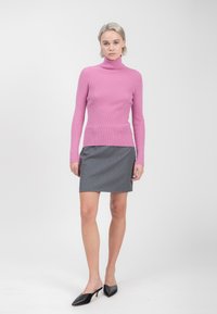 Maglione a collo alto rosa a coste abbinato a una gonna grigia con piccole pois bianchi e mule nere a punta.