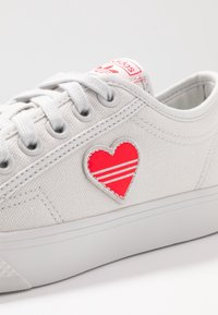 Grå kanvas sneakers med ett rött hjärtapplikation och tre vita ränder, grå snören och en vit gummisula.