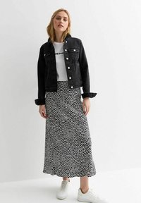Veste en denim noir, t-shirt blanc avec texte, jupe noir et blanc à motifs, baskets blanches. Coupe décontractée, boutons sur la veste, jupe longueur cheville.