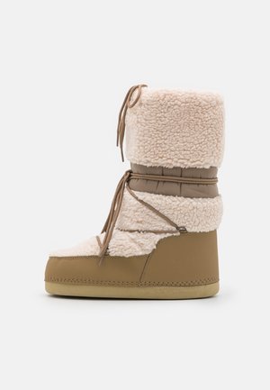 Botte d'hiver beige et crème avec une doublure épaisse en polaire, une tige rembourrée et une fermeture à lacets sur une semelle plate, vue de côté.